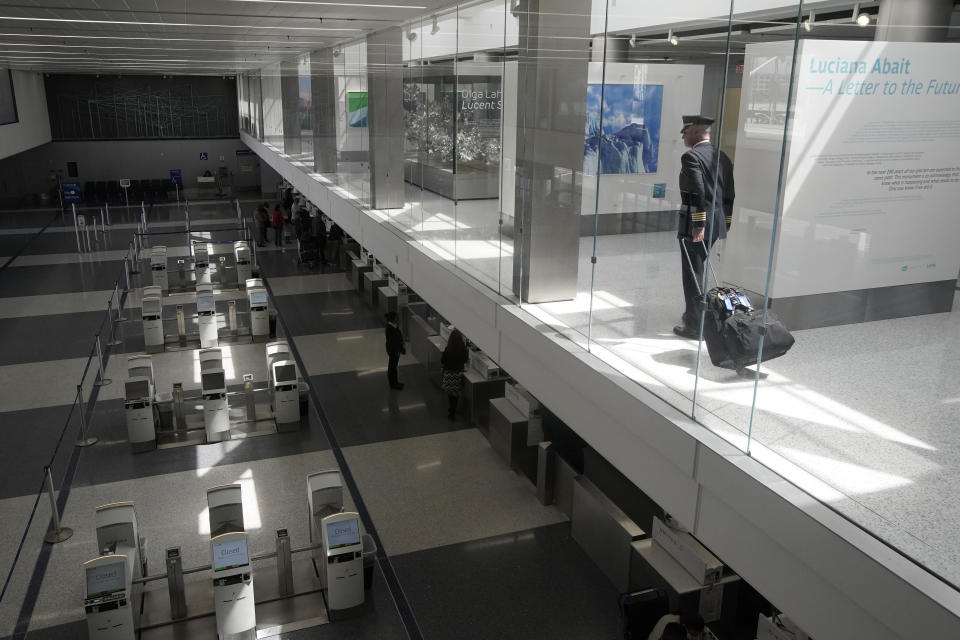 A pilot looks over sparse crowds at a check-in counter at the United terminal at Los Angeles International Airport, Tuesday, March 24, 2020, in Los Angeles. (AP Photo/Chris Carlson)