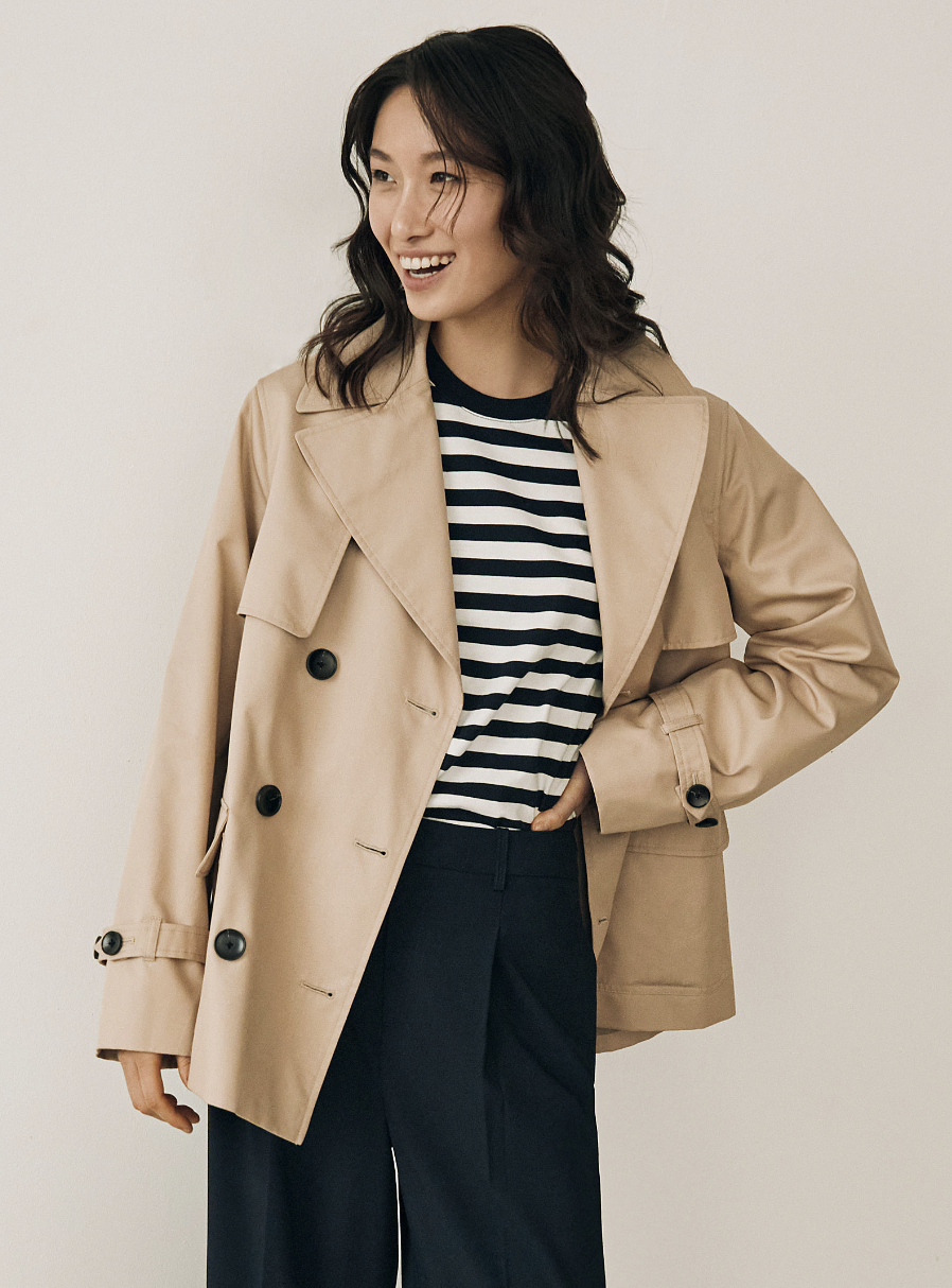 brunette model in blue pants, striped t-shirt and beige Cropped Double-Breasted Trench Coat (photo via Simons)