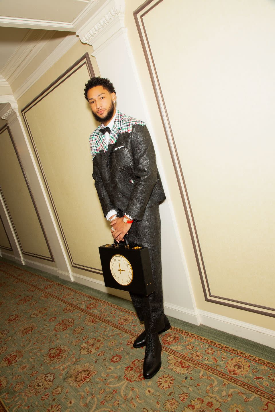 a man in a black coat and boots standing in front of a clock