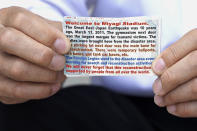 Olympic volunteer Atsushi Muramatsu shows business-card size flyers to express gratitude for support from overseas, during an interview with The Associated Press in Rifu, Japan, Thursday, July 29, 2021. He made the flyers to hand out to foreign media covering the 2020 Summer Olympics at Miyagi Stadium, where he is serving as a volunteer. (AP Photo/Chisato Tanaka)