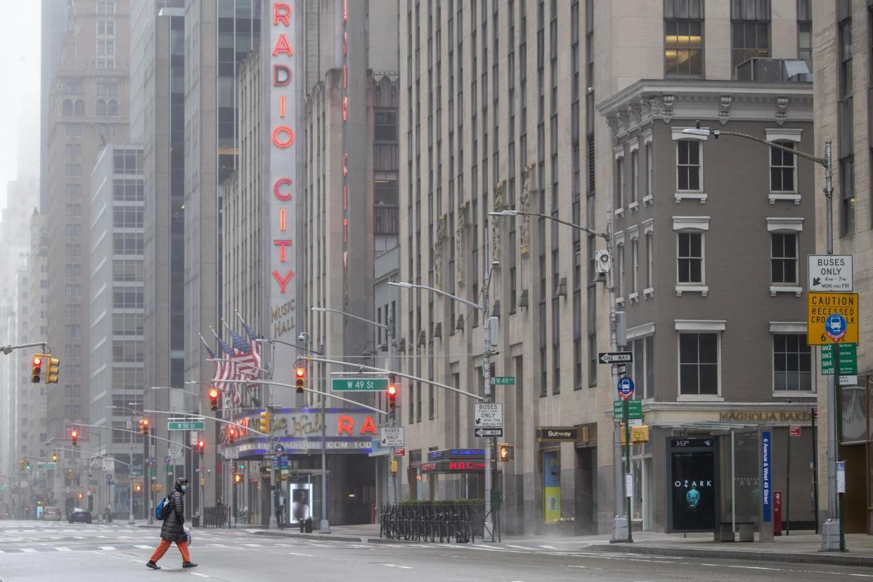 A woman wearing a facial mask makes her way across 6th Avenue near Radio City Music Hall, Sunday, March 29, 2020, in New York: AP