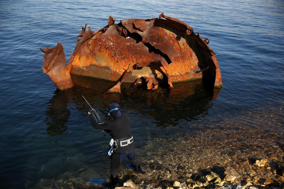 An amateur fisherman with speargun prepares to dive next to a part of shipwreck in Damari, an area with eleven shipwrecks, on Salamina island, west of Athens, on Thursday, Jan. 31, 2020. Greece this year is commemorating one of the greatest naval battles in ancient history at Salamis, where the invading Persian navy suffered a heavy defeat 2,500 years ago. But before the celebrations can start in earnest, authorities and private donors are leaning into a massive decluttering operation. They are clearing the coastline of dozens of sunken and partially sunken cargo ships, sailboats and other abandoned vessels. (AP Photo/Thanassis Stavrakis)