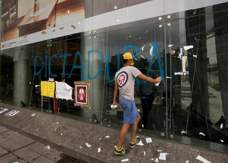 A man spray paints the Spanish word for "Dictatorship," on a glass facade of the United Nations headquarters in Caracas, Venezuela, Thursday, May 8, 2014. Hundreds of security forces broke up four camps maintained by student protesters, arresting 243 people in a Thursday pre-dawn raid. The camps consisting of small tents were installed more than a month ago in front of the UN building and other anti-government strongholds in the capital to protest against President Nicolas Maduro's government. (AP Photo/Fernando Llano)