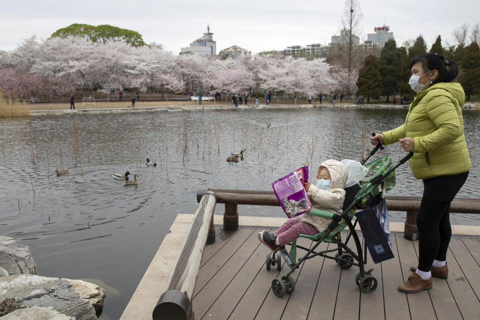 A woman pushes a child on a pram across from cherry blossoms at the Yuyuantan Park in Beijing on Thursday, March 26, 2020. While many of the city's world-famous tourist sites, including the sprawling Forbidden City ancient palace complex, remain closed, spring weather and budding cherry blossoms are coaxing outdoors citizens who have been largely confined to home for the last two months. For most people, the new coronavirus causes mild or moderate symptoms, such as fever and cough that clear up in two to three weeks. For some, especially older adults and people with existing health problems, it can cause more severe illness, including pneumonia and death. (AP Photo/Ng Han Guan)
