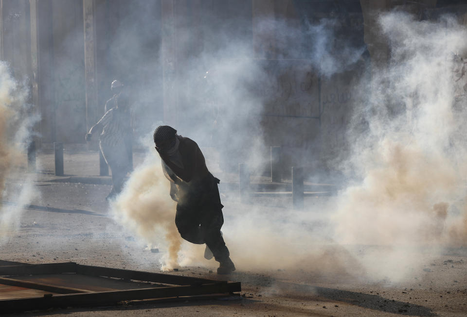 An anti-government protester runs from the smoke of tear gas, during clashes with riot police in Beirut, Lebanon, Saturday, Aug. 8, 2020. Dozens of Lebanese protesters stormed the buildings of a number of government ministries as well as the headquarters of the banking association. (AP Photo/Hussein Malla)