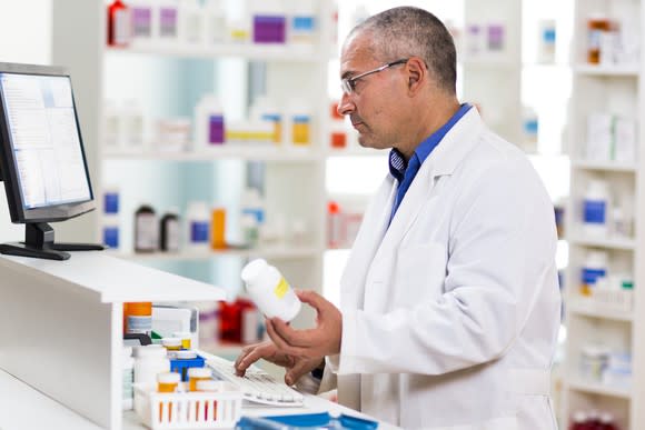 Pharmacist holds a pill bottle as he works on a computer.