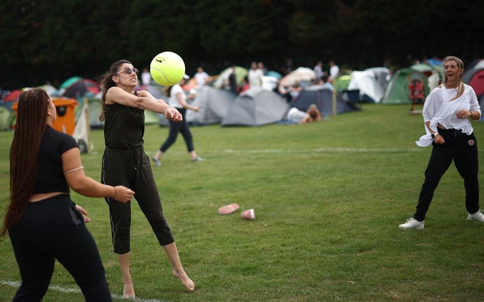 Fans play with a giant tennis ball, as they camp in The Queue