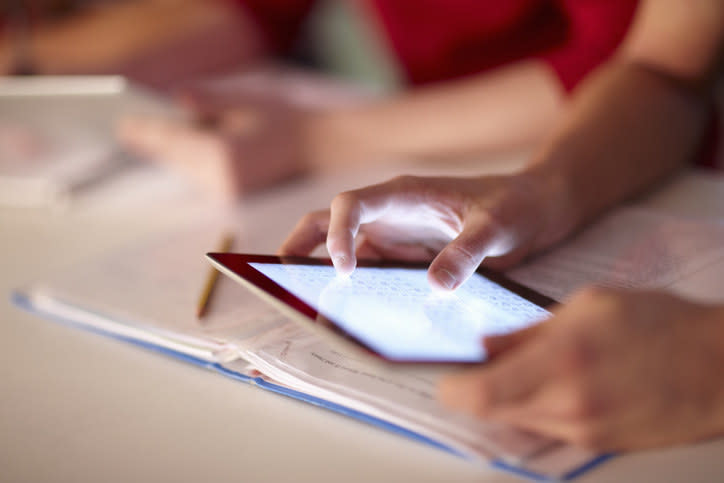 Fingers press a tablet in a classroom