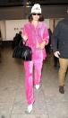 <p>In a hot pink velour suit, Giuseppe Zanotti white booties, white beanie, rectangular sunglasses and black handbag at London's Heathrow Airport.</p>