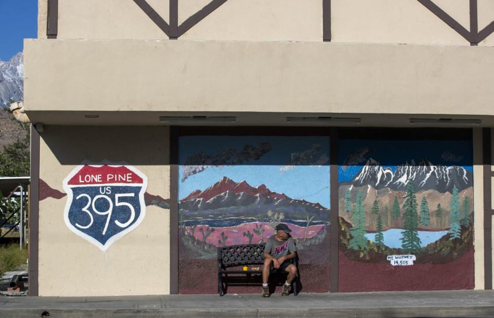 A man sits on a bench in front a building decorated with a mural of mountains