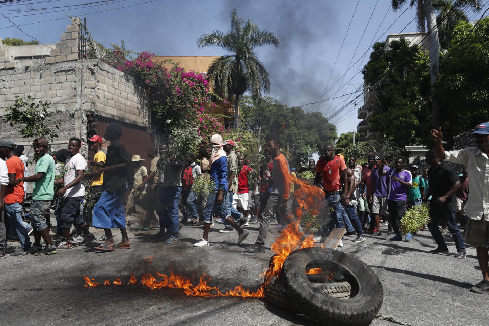 Demonstrators walk past a burning barricade during anti-government protests in Port-au-Prince, Haiti, Friday, Oct. 11, 2019. Protesters burned tires and spilled oil on streets in parts of Haiti's capital as they renewed their call for the resignation of President Jovenel Moïse just hours after a journalist was shot to death. (AP Photo/Rebecca Blackwell)