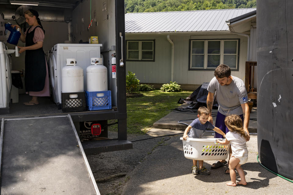 Image: Dillion Hall, right, and his two children, carry a basket of clothes to a laundry truck in downtown Buckhorn, Ky. on Aug. 19, 2022. (Michael Swensen for NBC News)