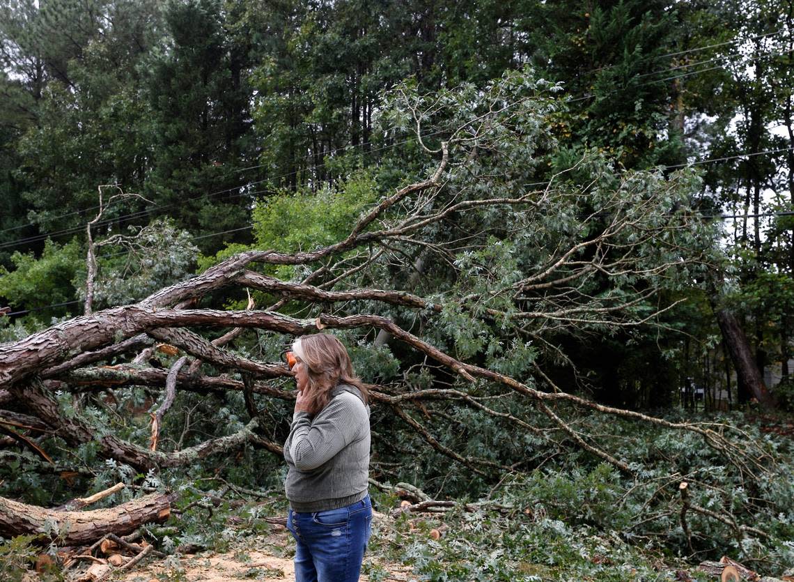 Cathy Hummel stands next to a downed tree that blocks Bivins Road following Tropical Storm Ian on Saturday, Oct. 1, 2022, in Durham, N.C.