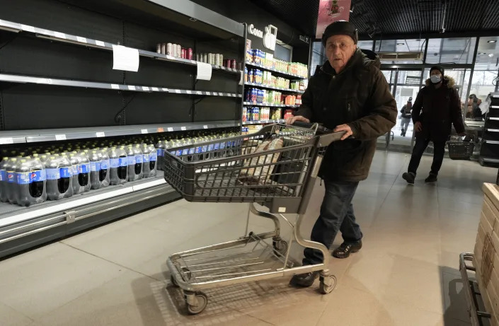 A man pushes a shopping cart past nearly empty shelves at a grocery store.