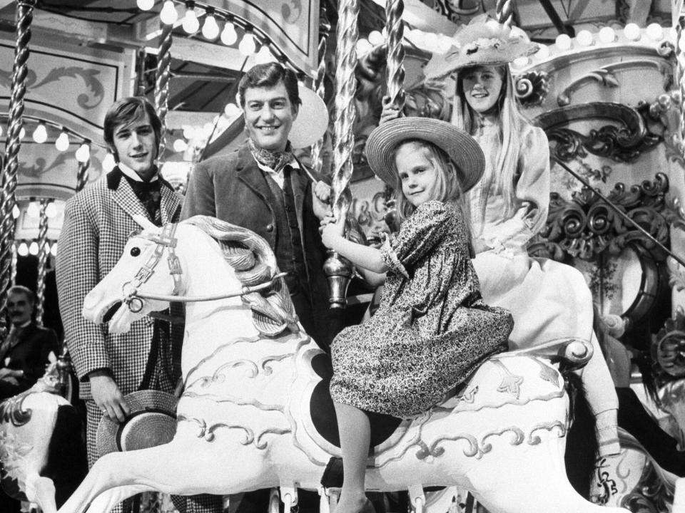 Six-year-old CARRIE BETH and her sister STANCEY, 13, steal the scene here from their brother BARRY, 16, and father DICK VAN DYKE, who watch as the girls go round the merry-go-round at Pinewood Studios