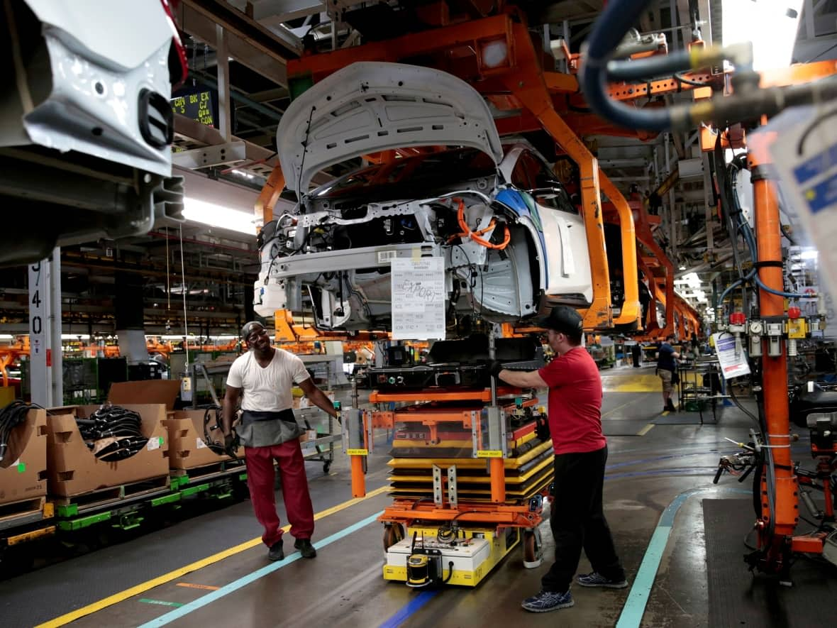 GM workers in Michigan connect a battery pack underneath a partially assembled 2018 Chevrolet Bolt EV in 2018. (Rebecca Cook/Reuters - image credit)