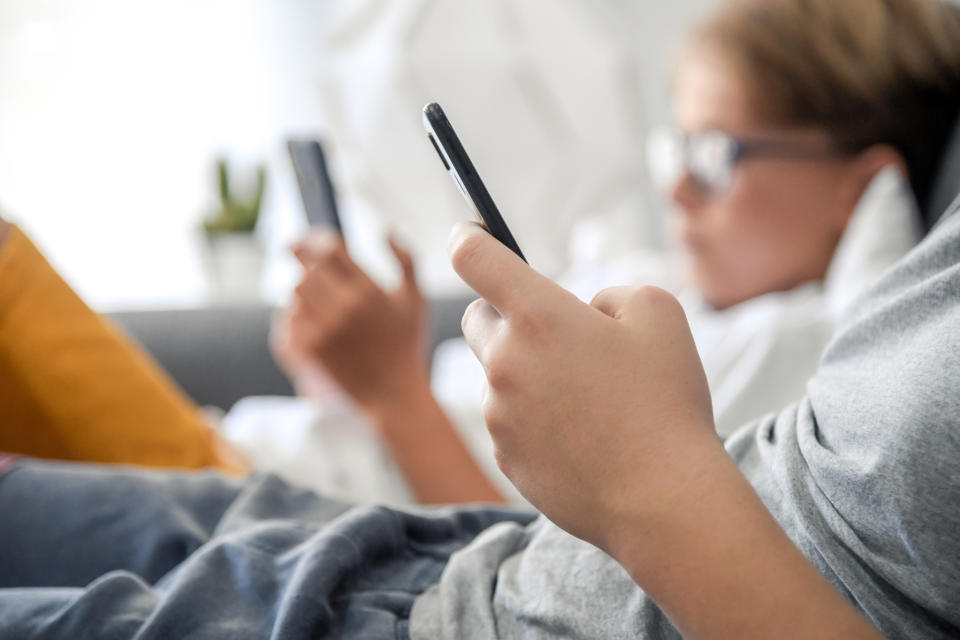 Two boys hold phones while sitting on a sofa.