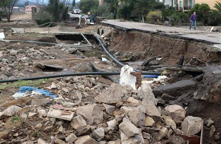 People walk on a damaged road following extreme rainfall near Olbia on Sardinia island November 20, 2013. REUTERS/Tony Gentile