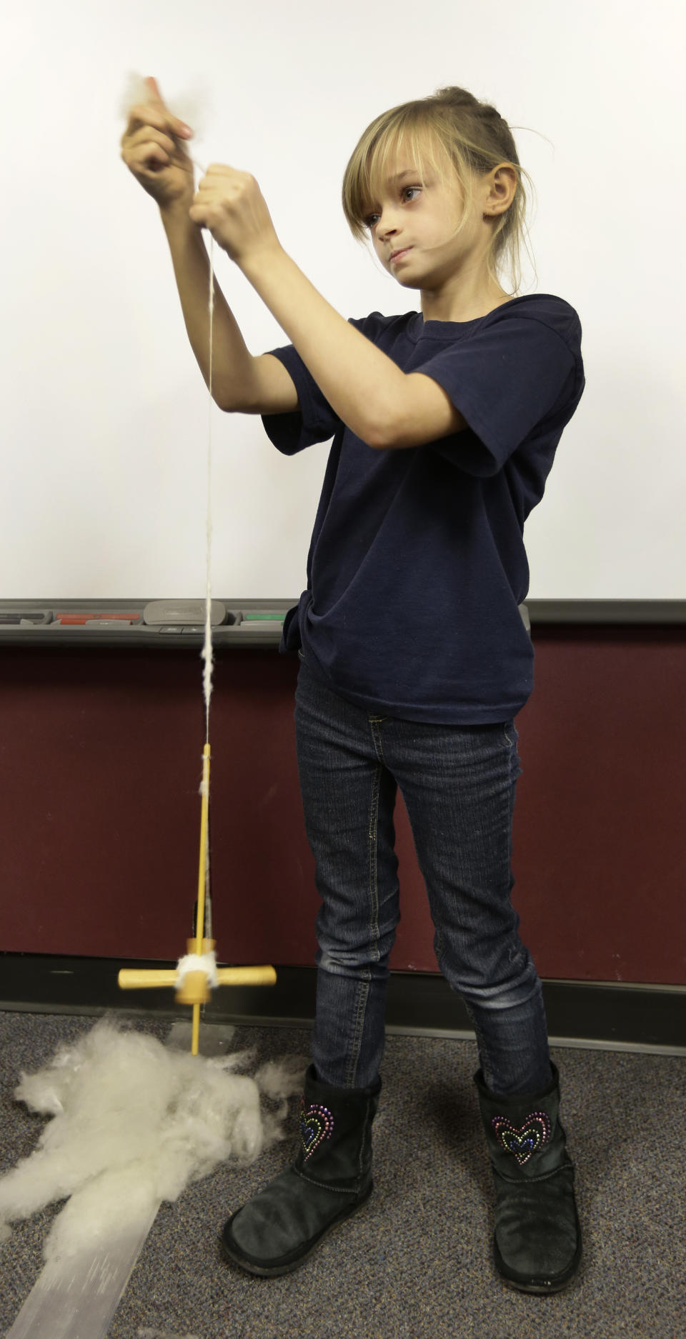 In this Thursday, Dec. 12, 2013 photo, fourth grader Ally Jones uses a drop spindle to make yarn from spun wool at the Walton 21st Century Rural Life Center in Walton, Kan. Fourth graders at the agriculture-focused charter school are responsible for the school's sheep, and than learn to make products from wool. (AP Photo/Charlie Riedel)