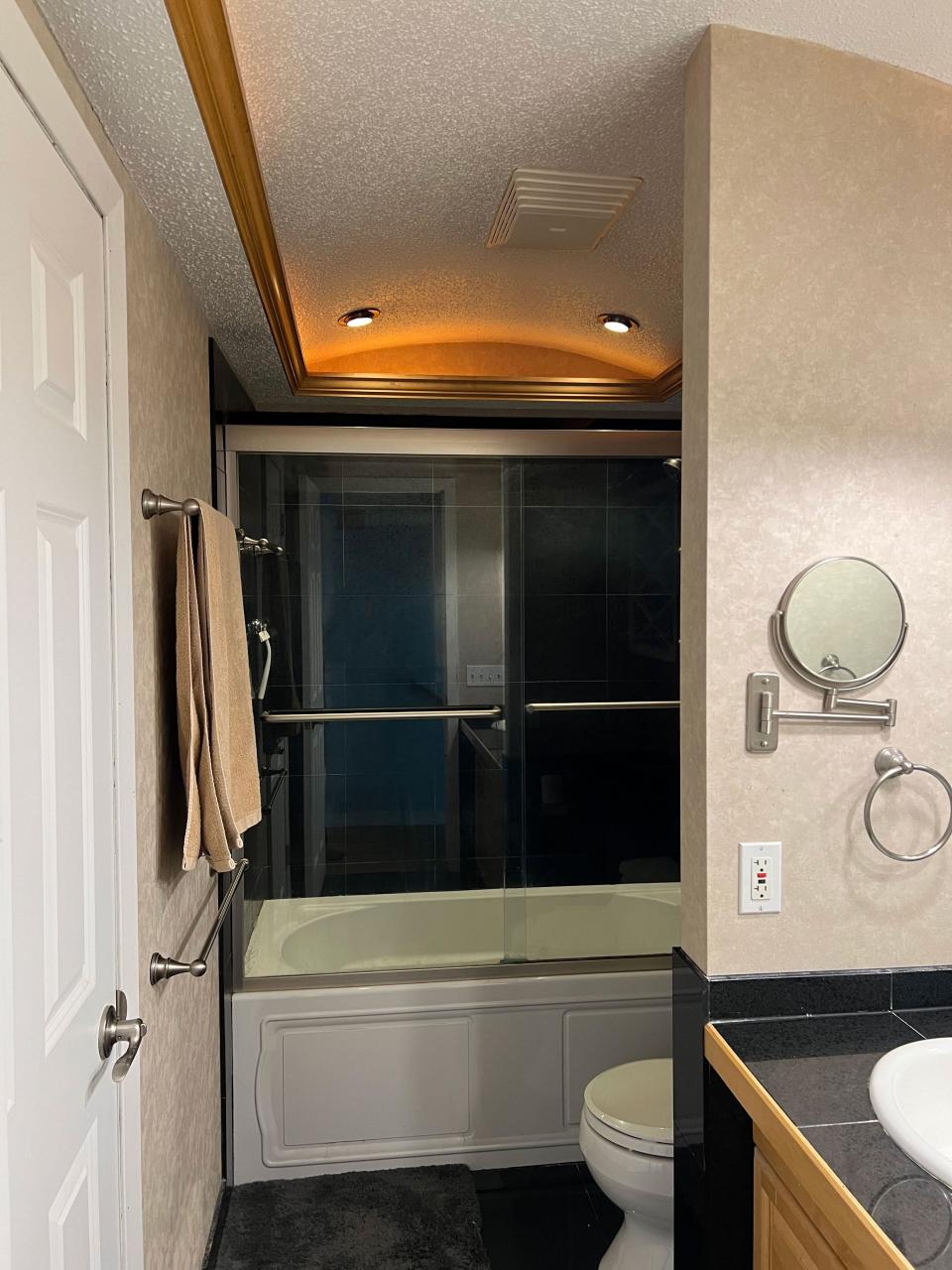 A softly lit small bathroom with black tile and a curved tray ceiling.