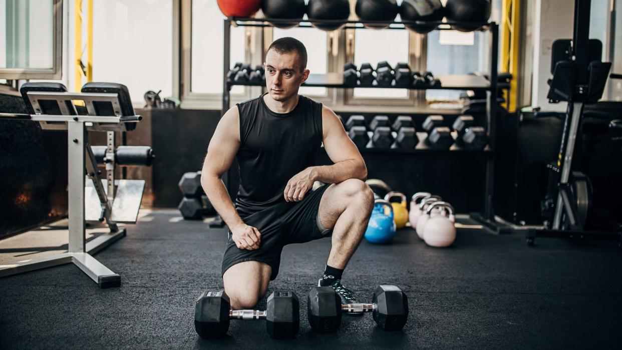  A man in the gym standing next to a pair of dumbbells. 