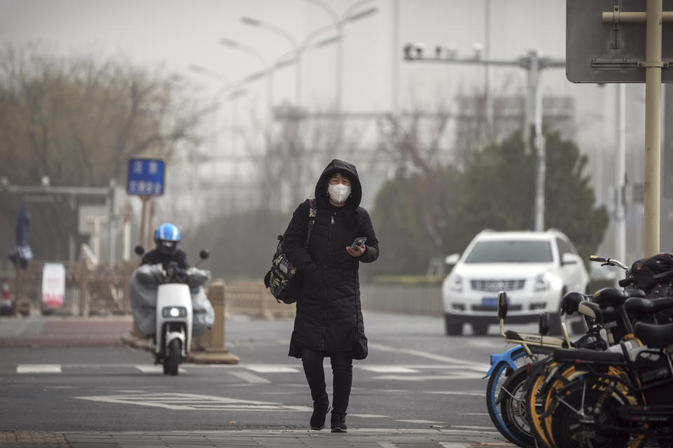 A woman wearing a face mask walks on a street in Beijing, Monday, Dec. 12, 2022, as capital city is hit by sandstorm. China will drop a travel tracing requirement as part of an uncertain exit from its strict "zero-COVID" policies that have elicited widespread dissatisfaction. (AP Photo/Andy Wong)