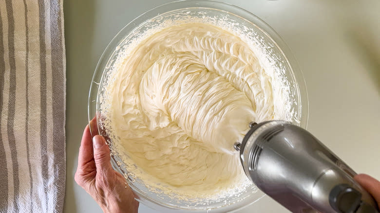 Whipping mascarpone cream with hand mixer in glass bowl