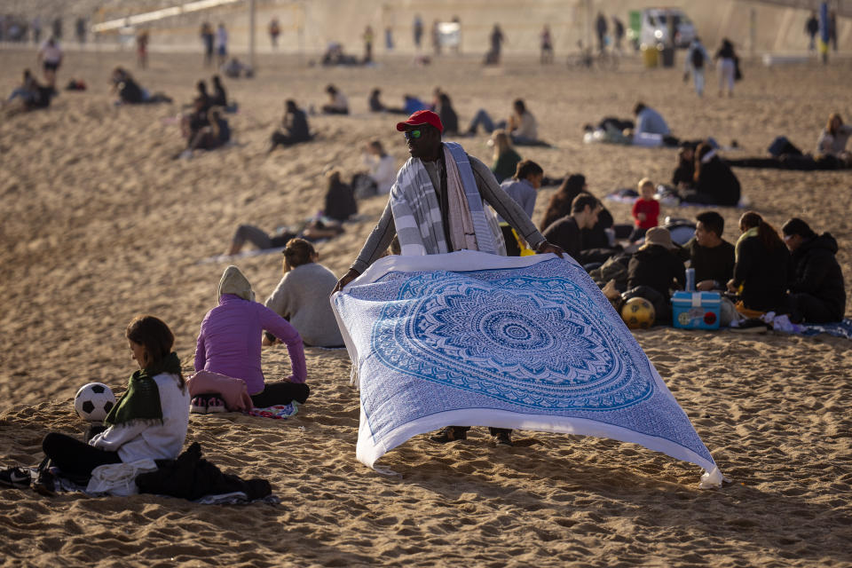 FILE - A street vendor displays sheets for sale while people sunbathe on the beach in Barcelona, Spain, Jan. 26, 2024. For the eighth straight month, Earth was record hot, according to the European climate agency’s analysis of January 2024. (AP Photo/Emilio Morenatti, File)