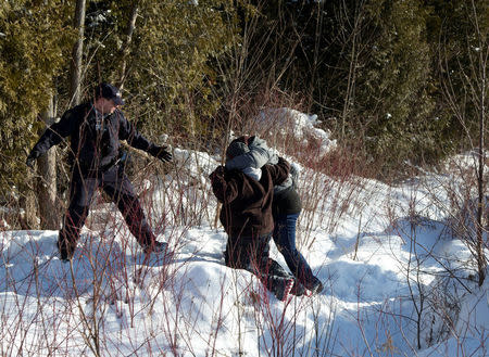 A Royal Canadian Mounted Police (RCMP) officer waits as a woman helps another across the U.S.-Canada border into Hemmingford, Canada, from Champlain in New York, U.S., February 17, 2017. REUTERS/Christinne Muschi