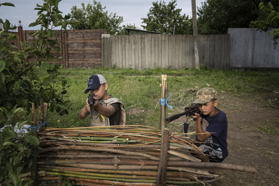 Maksym and Andrii, 11 years old boys, play with plastic guns at a self-made checkpoint on the highway in Kharkiv region, Ukraine, Wednesday, July 20, 2022. (AP Photo/Evgeniy Maloletka)