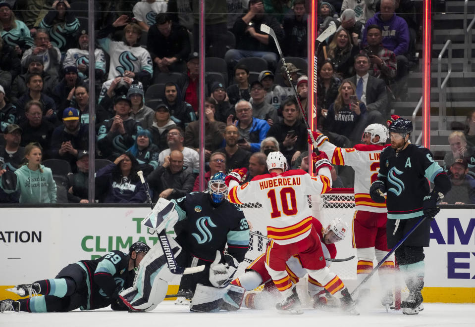 Calgary Flames left wing Andrew Mangiapane (88) falls in the goal after scoring as teammates Jonathan Huberdeau (10) and Elias Lindholm (28) react while Seattle Kraken goaltender Joey Daccord (35) and defenseman Adam Larsson, far right, look away during the third period of an NHL hockey game Monday, Nov. 20, 2023, in Seattle. The Flames won 4-3 in overtime. (AP Photo/Lindsey Wasson)