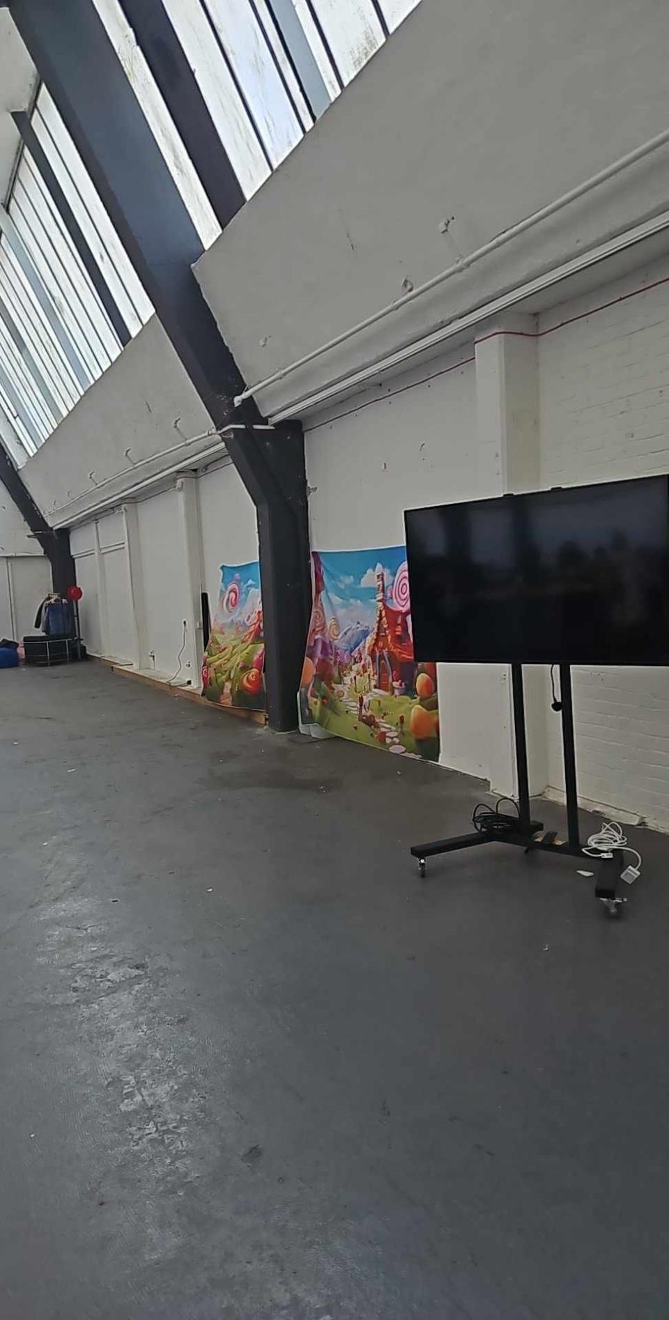 A small mural of animated characters on a wall behind an empty black rolling TV stand in an otherwise barren indoor space