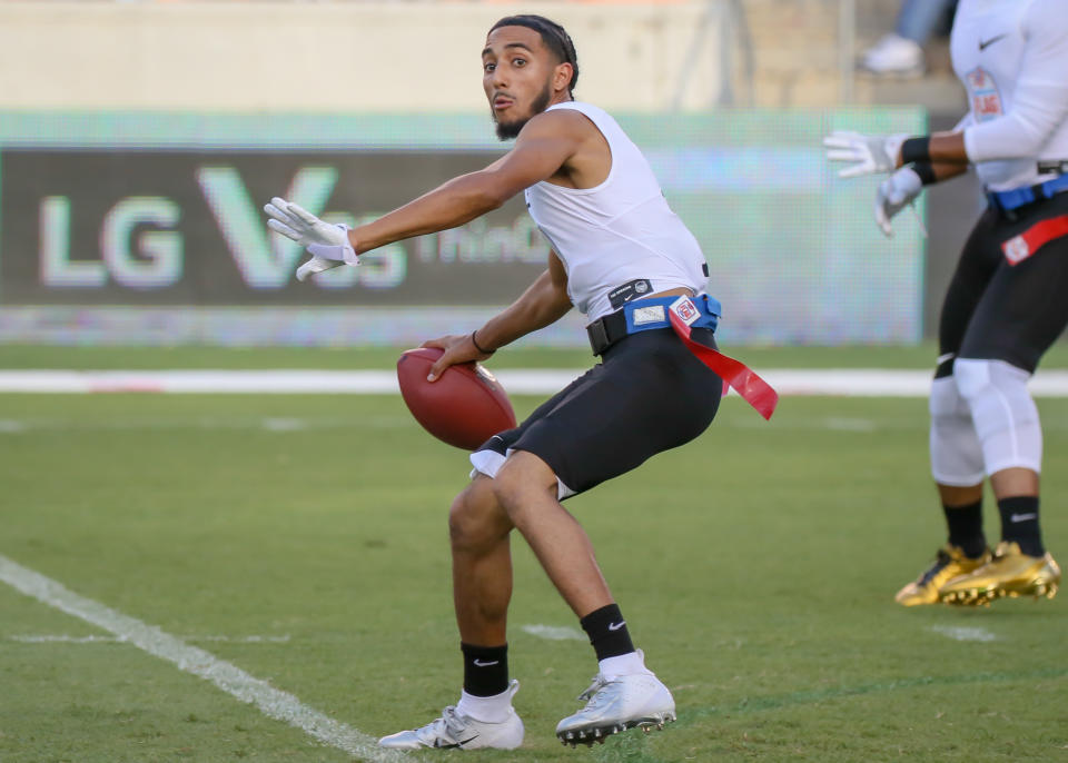 Soccer player in action on the field, wearing black sports shorts, a white sleeveless shirt and soccer shoes, holding a soccer ball. Name unknown