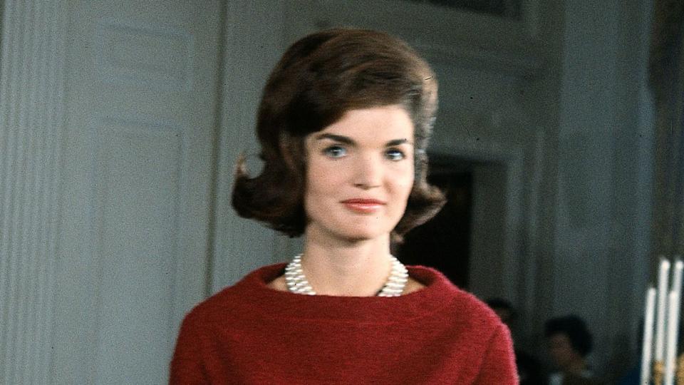 First Lady Jacqueline Kennedy (1929 - 1994), in a red dress, stands in before a dining room table in the White House during the filming of a CBS News Special program called 'A Tour of the White House with Mrs. John F. Kennedy,' Washington DC, January 15, 1962