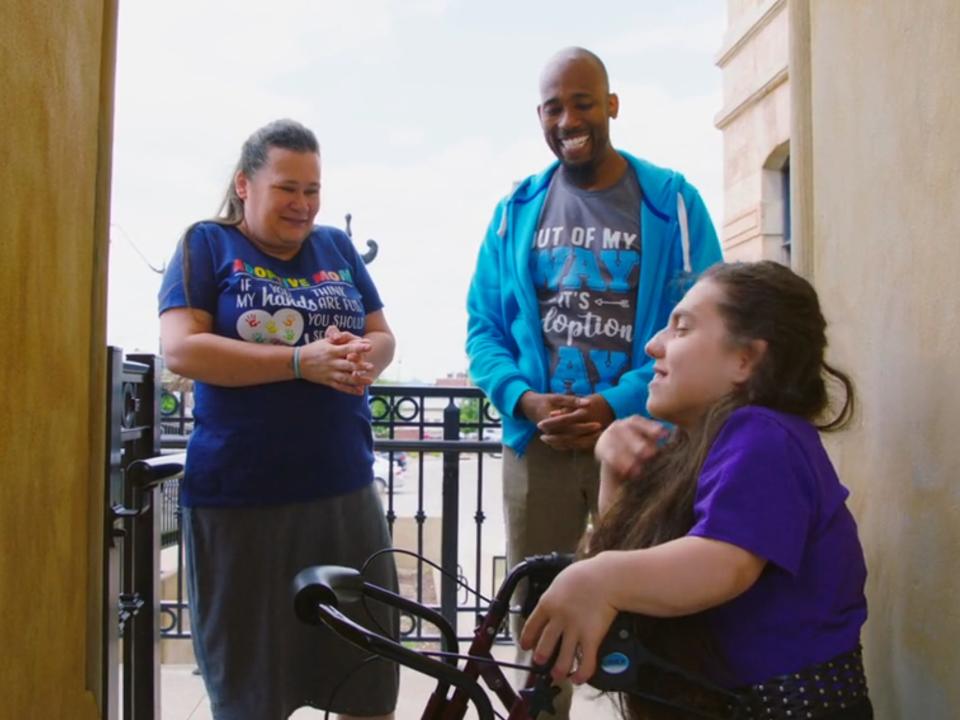 natalia grace barnett stands with antwon mans and cynthia mans, who are both smiling and wearing t-shirts that read "out of my way it's adoption day" and "adoptive mom"