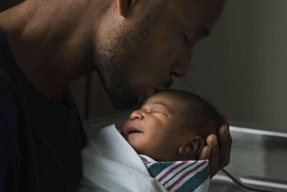 A father kissing forehead of newborn son.