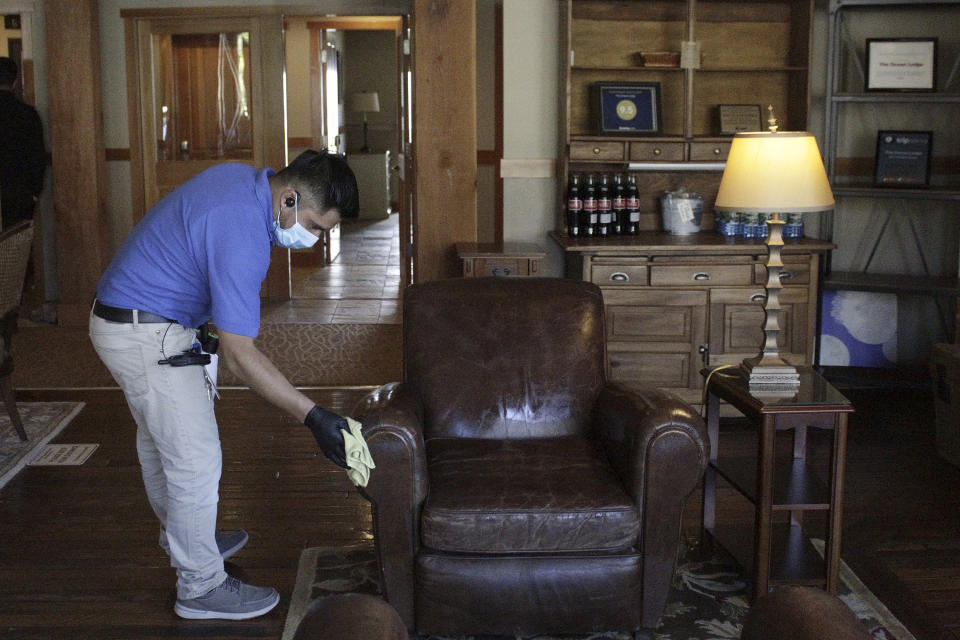 In this Thursday, May 28, 2020, photo, Aroldo Ramos, an employee at The Ocean Lodge, wipes down furniture in the hotel lobby with disinfectant in Cannon Beach, Ore. The Ocean Lodge welcomed guests back starting last week after an extended shut-down of all hotels and vacation rentals in the small beach town to prevent the spread of the new coronavirus. With summer looming, Cannon Beach and thousands of other small, tourist-dependent towns nationwide are struggling to balance fears of contagion with their economic survival in what could be a make-or-break summer. (AP Photo/Gillian Flaccus)