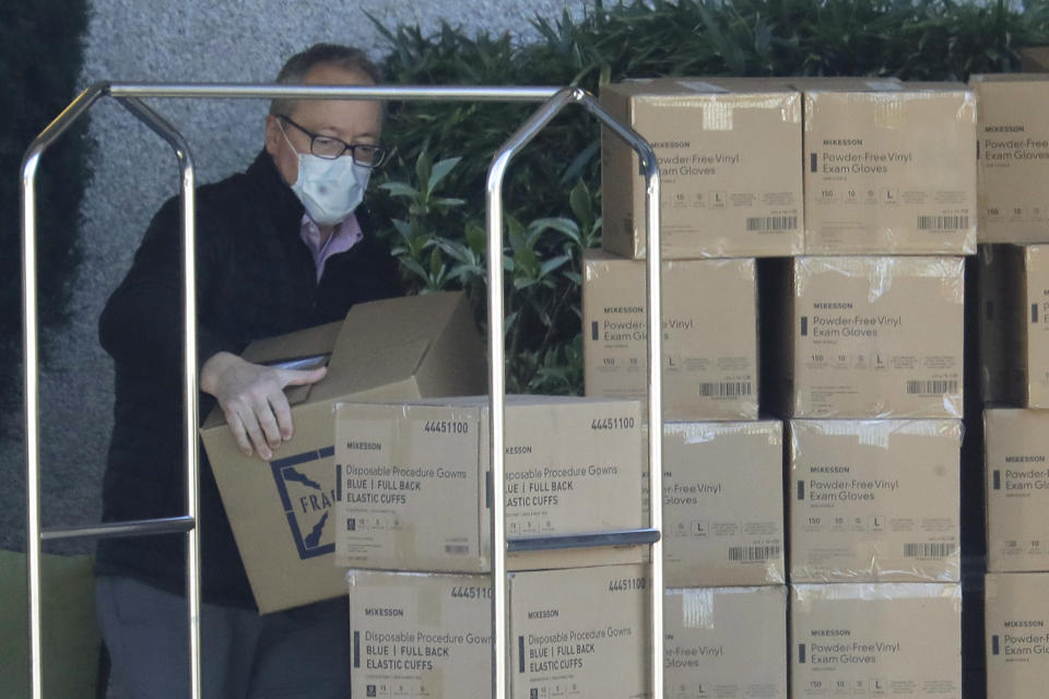 A worker wears a mask as he loads new supplies of gloves, gowns, and other protective gear onto a cart at the Life Care Center in Kirkland, Wash. Monday, March 9, 2020, near Seattle. The nursing home is at the center of the outbreak of the COVID-19 coronavirus in Washington state. (AP Photo/Ted S. Warren)