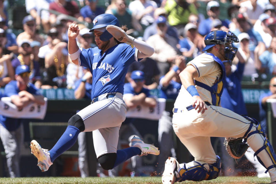 Toronto Blue Jays' Bo Bichette, left, scores on a Alejandro Kirk sacrifice fly as Seattle Mariners catcher Cal Raleigh, right, waits for the throw during the fourth inning of a baseball game, Sunday, July 7, 2024, in Seattle. (AP Photo/Jason Redmond)