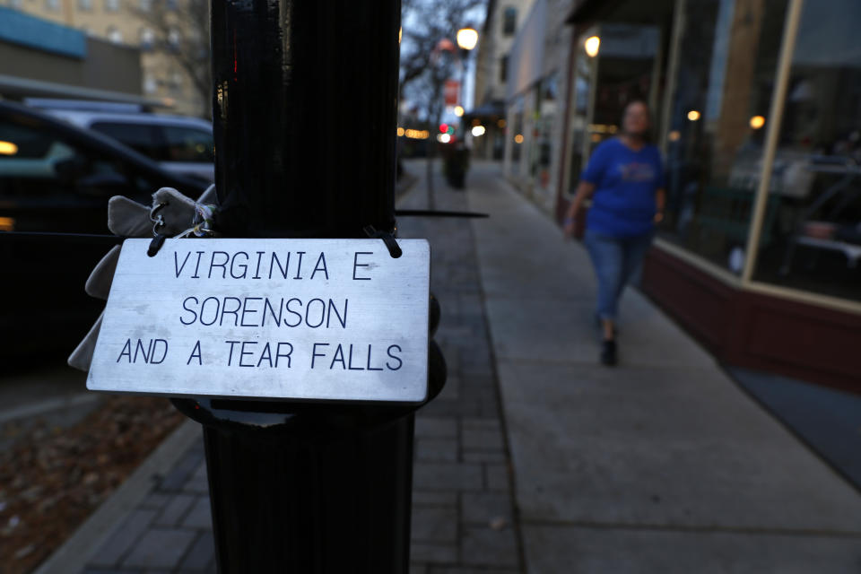 A plaque honoring Virginia “Ginny” Sorenson rests on a lamp post on Thursday, Nov. 3, 2022, along Main Street in Waukesha, Wis., as Donna Kalik walks nearby. Sorenson was a leader and member of the Milwaukee Dancing Grannies who was killed when the driver of an SUV sped through a Christmas parade in Waukesha last November, killing six and injuring dozens of other people. There is a plaque for each of the dead along the parade route. Several new members have joined the Grannies since the incident, including Kalik, who has become the group’s volunteer coordinator. She was at the parade last year and felt compelled to support the Grannies. “It was like a war zone,” she said of the scene the driver left in his wake. (AP Photo/Martha Irvine)