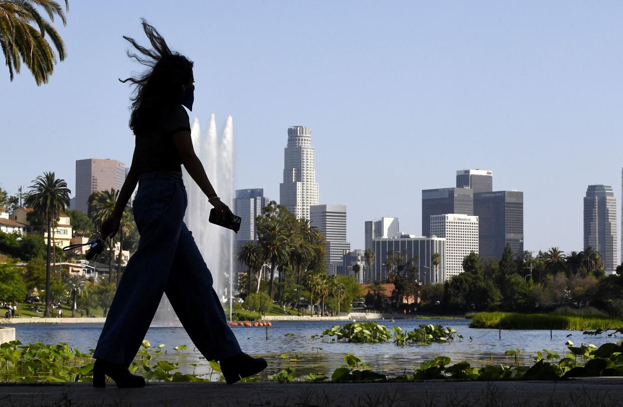 A woman walks at Echo Park Lake with downtown Los Angeles in the background on Saturday, May 23, 2020, during the coronavirus pandemic. California Gov. Gavin Newsom has approved 45 of the state's 58 counties to reopen some businesses since May 8 when he loosened his original mid-March stay-at-home order.