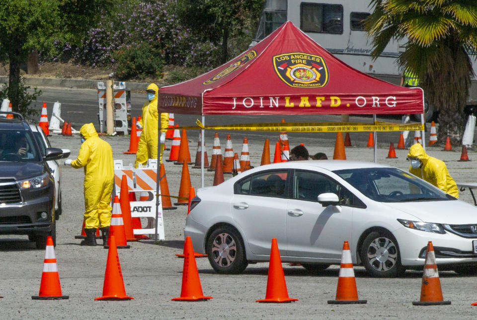 Los Angeles Fire Department officials wearing protective gear deliver testing kits to a waiting motorists at a COVID-19 drive-up testing site in Elysian Park, Los Angeles Thursday, April 2, 2020. Officials say hand-washing and keeping a safe social distance are priorities in battling the COVID-19 virus. (AP Photo/Damian Dovarganes)
