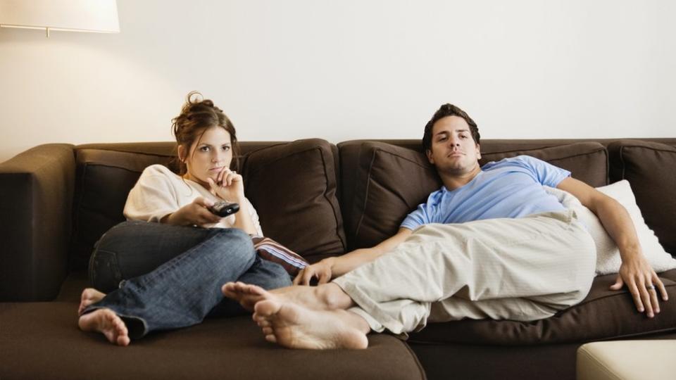 No ejercicio. Una mujer y un hombre echados en un sofá mirando televisión