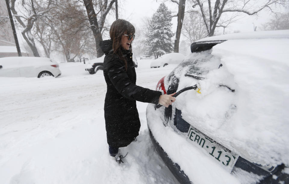 Carli Webber of Denver clears off her sports-utility vehicle to head to work as a storm packing snow and high winds sweeps in over the region Tuesday, Nov. 26, 2019, in Denver. Stores, schools and government offices were closed or curtailed their hours while on another front, Thanksgiving Day travellers were forced to wrestle with snow-packed roads and flight delays or cancellations throughout the intermountain West. (AP Photo/David Zalubowski)