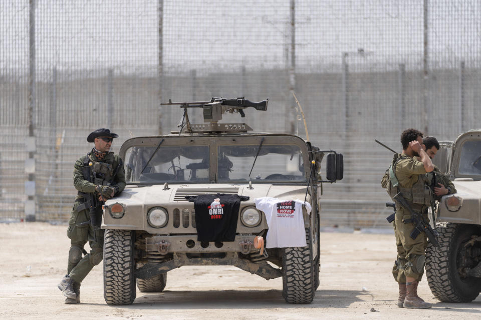 Israeli soldiers stand near their vehicles, displaying t-shirts calling for the return of hostages, on the Israeli side of the Erez crossing into the Gaza Strip from southern Israel as trucks carrying humanitarian aid supplies bound for the Gaza Strip are inspected, Wednesday, May 1, 2024. (AP Photo/Ohad Zwigenberg)