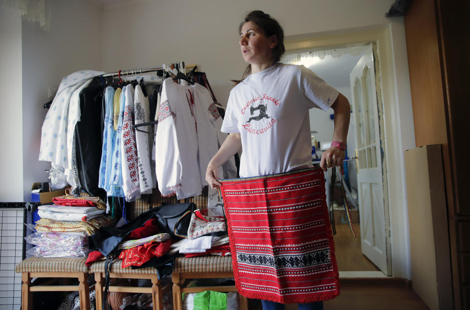 In this picture taken Tuesday, May 21, 2019, Valentina Radu shows traditional clothing items she produces in Luncavita, Romania. Radu also worked in Italy, but when her husband lost his job there, they struggled to pay the rent and decided to come home where they used European Union funds to buy a small farm and she further opened a tailor's shop. (AP Photo/Vadim Ghirda)