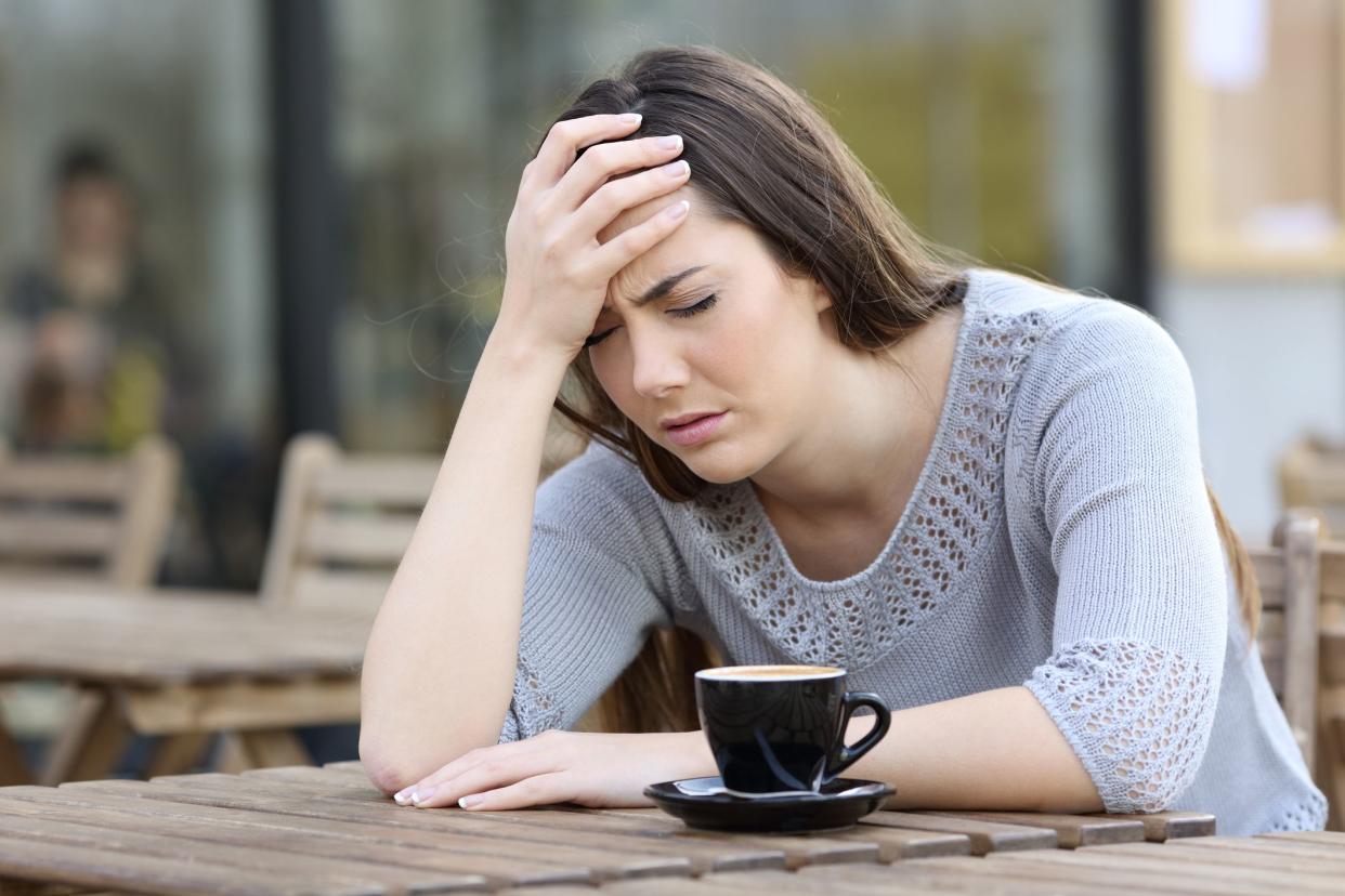 Depressed girl complaining alone with hand on head on a coffee shop terrace