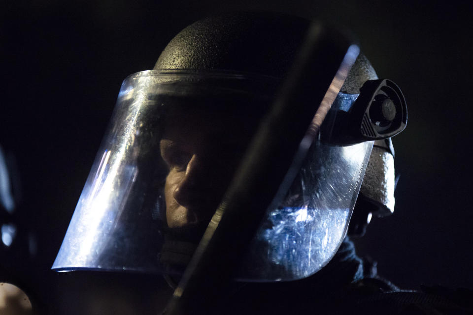 A Portland police officer watches a crowd of protesters at the Laurelhurst neighborhood early in the morning on Saturday, Aug. 8, 2020 in Portland, Ore. (AP Photo/Nathan Howard)