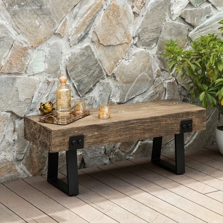 Avant garde wood-and-metal garden bench in front of a stone wall.