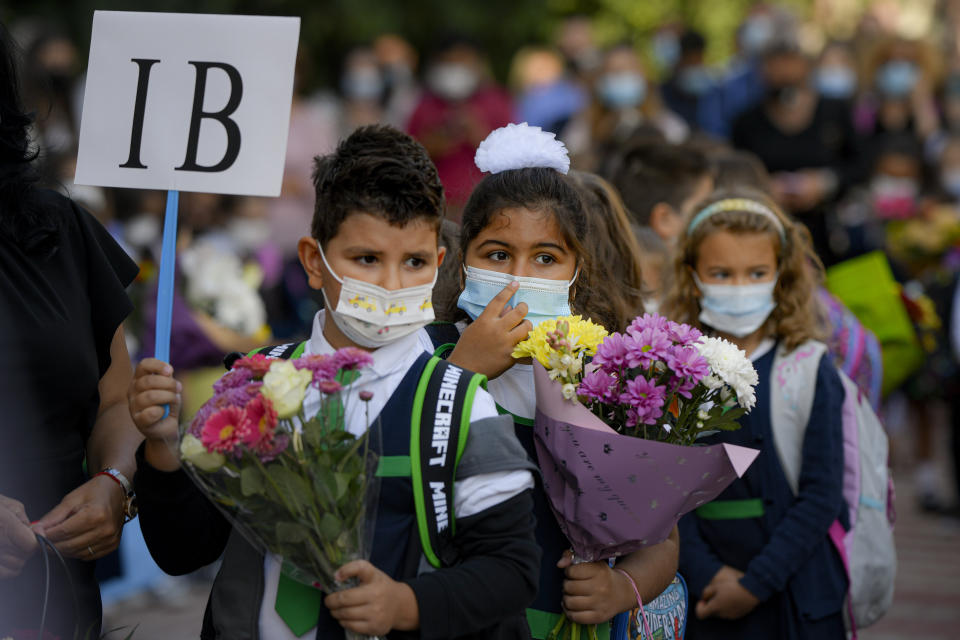 Children wearing face masks hold flowers during festivities marking the beginning of the school year at a school in Bucharest, Romania, Monday, Sept. 13, 2021. Children returned to classrooms in Romania, a country with one of the lowest COVID-19 vaccination rates in the European Union, as the daily infection numbers continue to rise. (AP Photo/Andreea Alexandru)